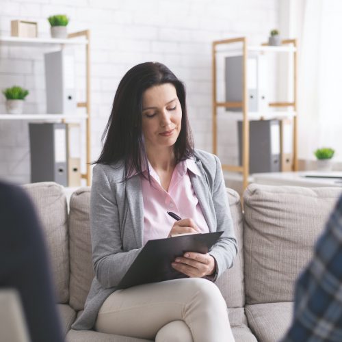 Professional psychologist taking notes at couple meeting with patients